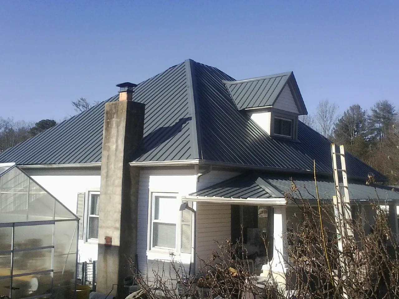 Dark blue standing seam metal roof on a white farmhouse with dormer — Slate & Tile Roof Repair by Roofing Brothers in Maxatawny