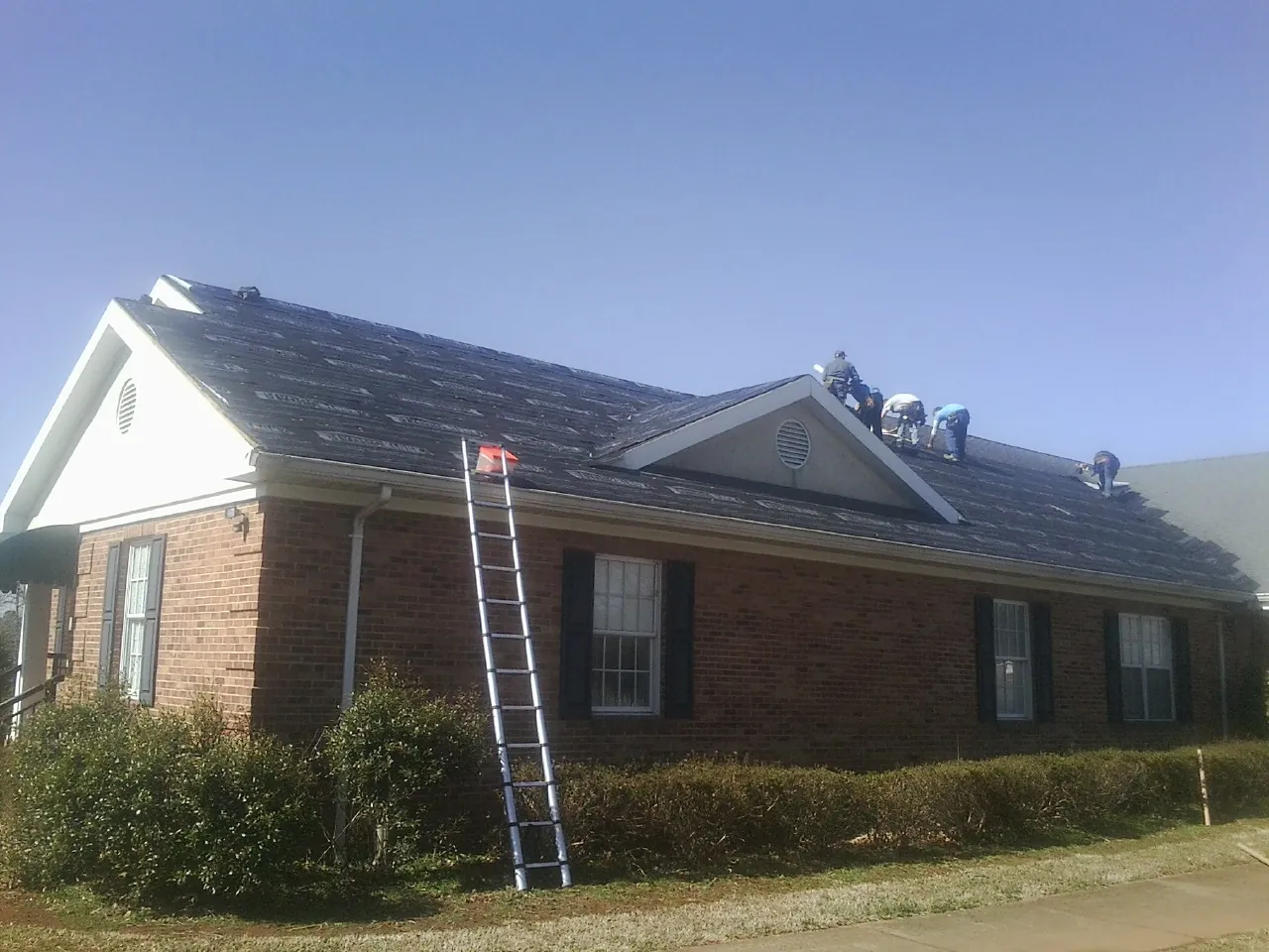 Crew tearing shingles off a brick ranch roof with a ladder set — Emergency Roof Repair work by our crew in Maxatawny