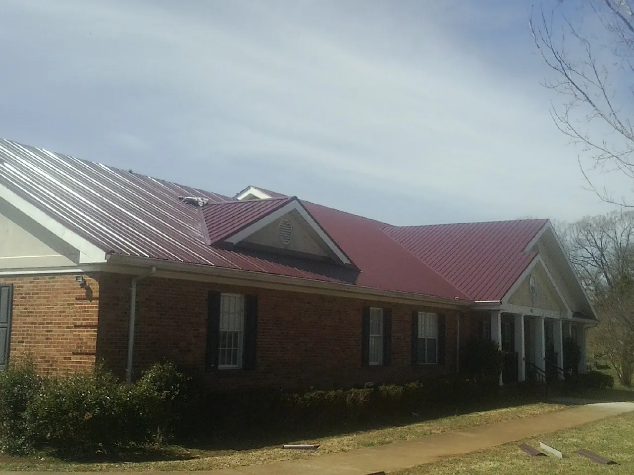 Red metal roof with gabled entries on a long brick building, from a Hail Damage Roof Repair job in Maxatawny