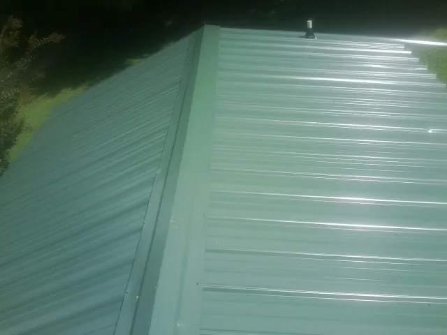 New green metal panels meeting at the ridge of a roof — Flat Roof Repair work by our crew in Maxatawny