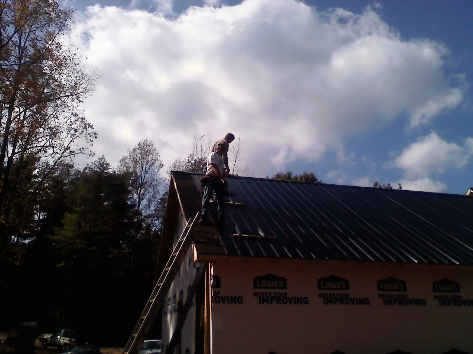 Roofer fastening dark metal panels high against a cloudy sky, from a Roof Inspection job in Maxatawny
