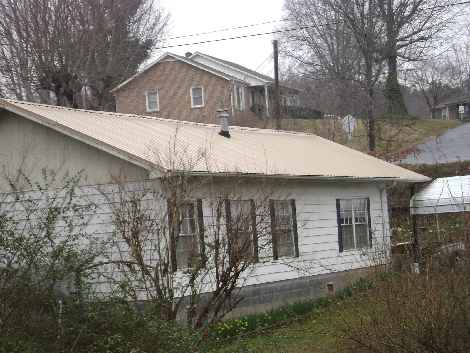 Tan metal roof on a white sided house set into a hillside — Commercial Roofing by Roofing Brothers in Maxatawny